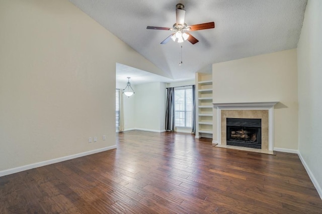 unfurnished living room with dark wood-type flooring, ceiling fan, a textured ceiling, a tiled fireplace, and vaulted ceiling