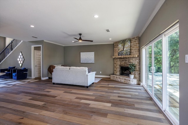 living room featuring hardwood / wood-style flooring, a fireplace, ornamental molding, and ceiling fan