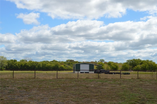 view of yard featuring fence, an outbuilding, a rural view, and a detached garage