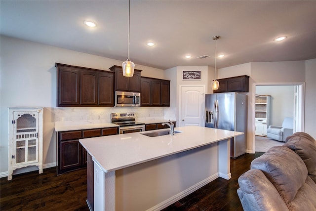 kitchen with pendant lighting, sink, a kitchen island with sink, dark brown cabinets, and stainless steel appliances