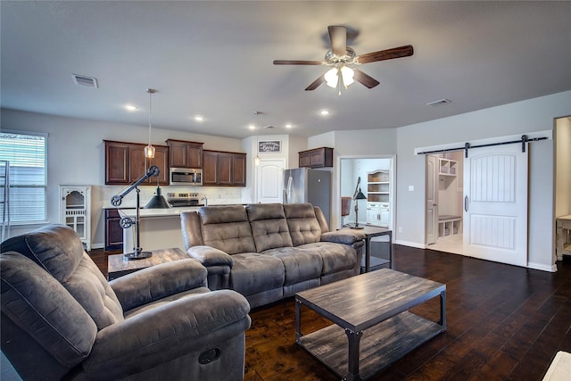 living room featuring dark hardwood / wood-style flooring, a barn door, and ceiling fan