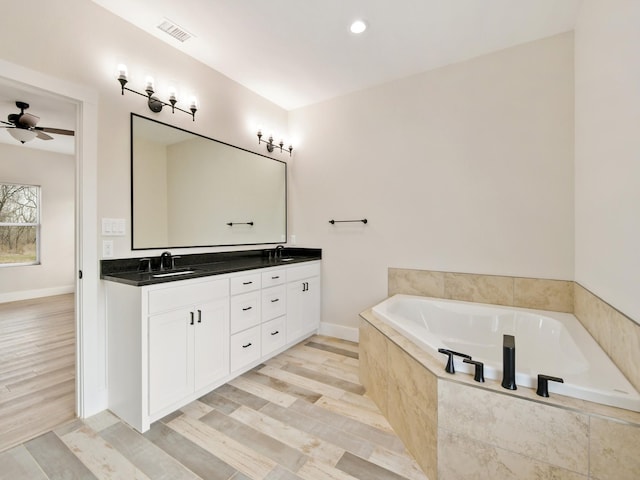 bathroom featuring vanity, tiled tub, wood-type flooring, and ceiling fan