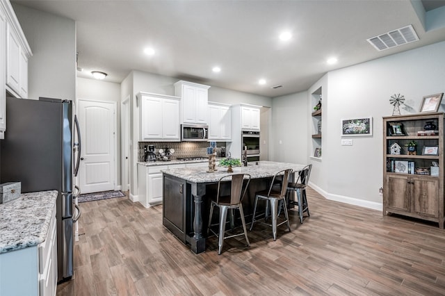 kitchen with a kitchen bar, white cabinetry, appliances with stainless steel finishes, light stone countertops, and a kitchen island with sink