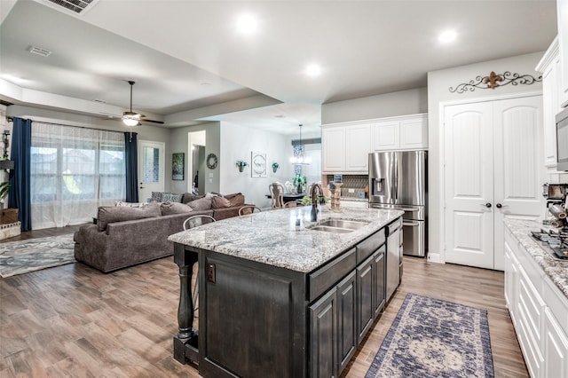 kitchen with appliances with stainless steel finishes, sink, white cabinets, light stone countertops, and a center island with sink