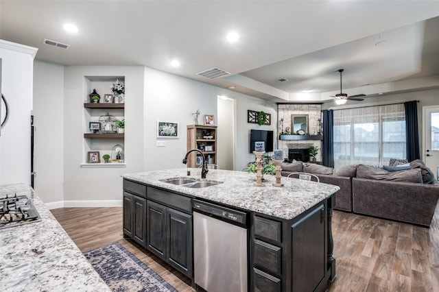 kitchen featuring a kitchen island with sink, light stone countertops, stainless steel dishwasher, and sink