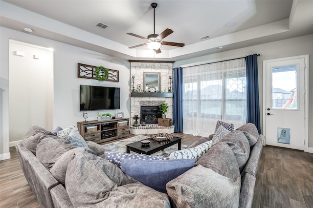 living room with hardwood / wood-style flooring, a fireplace, a raised ceiling, and ceiling fan