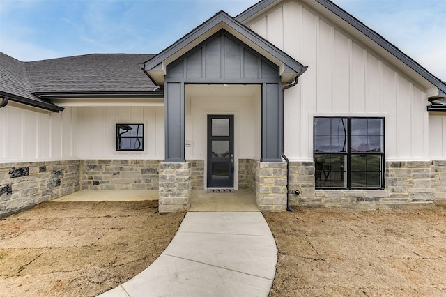 entrance to property with stone siding, a shingled roof, and board and batten siding