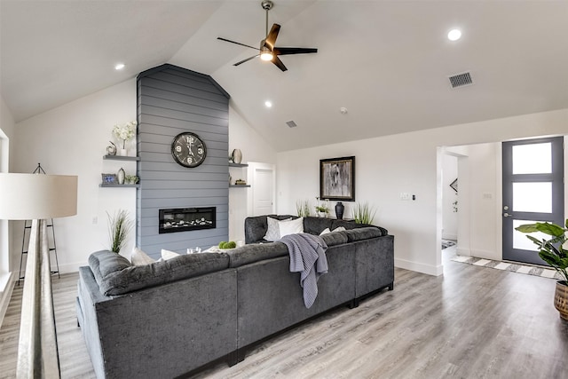 living area featuring a fireplace, visible vents, vaulted ceiling, ceiling fan, and light wood-type flooring