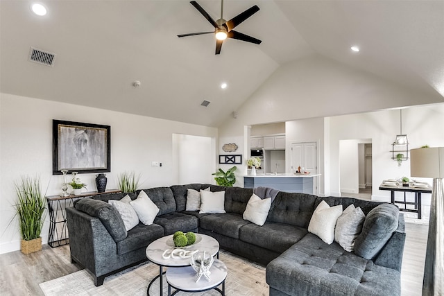 living area with ceiling fan, high vaulted ceiling, light wood-type flooring, and visible vents