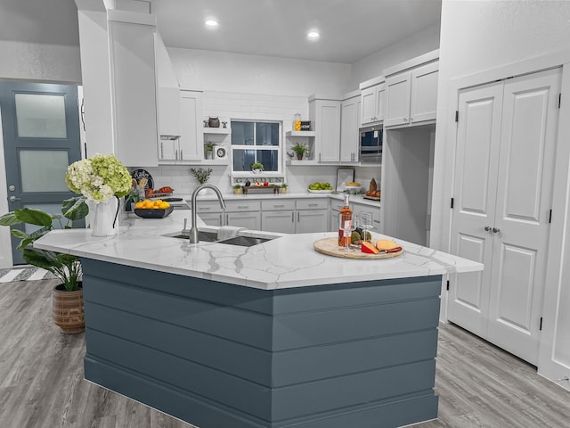 kitchen featuring stainless steel microwave, a peninsula, light stone countertops, open shelves, and a sink