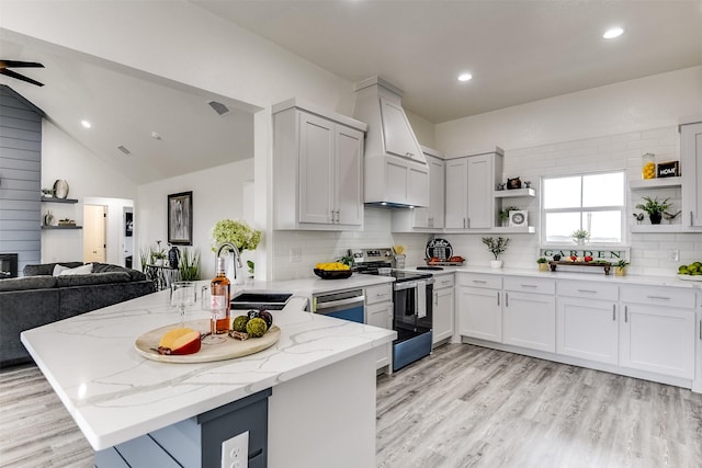 kitchen featuring appliances with stainless steel finishes, open floor plan, a peninsula, light stone countertops, and a sink