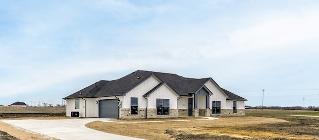 modern farmhouse style home with central AC unit, a garage, driveway, stone siding, and board and batten siding