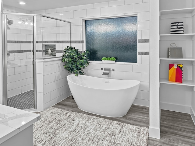 full bath featuring a stall shower, wood finished floors, a freestanding bath, vanity, and tile walls