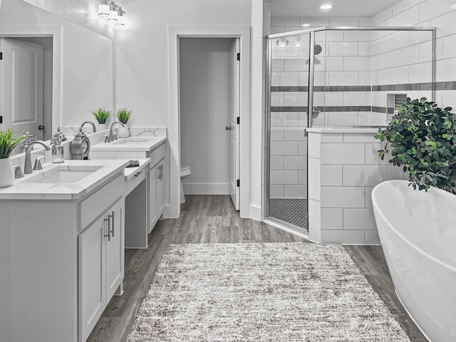 bathroom featuring a freestanding bath, toilet, vanity, a shower stall, and wood finished floors