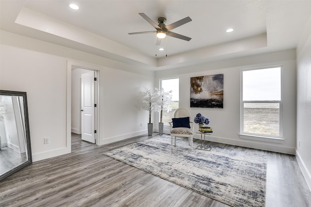 sitting room with wood finished floors, a raised ceiling, and baseboards