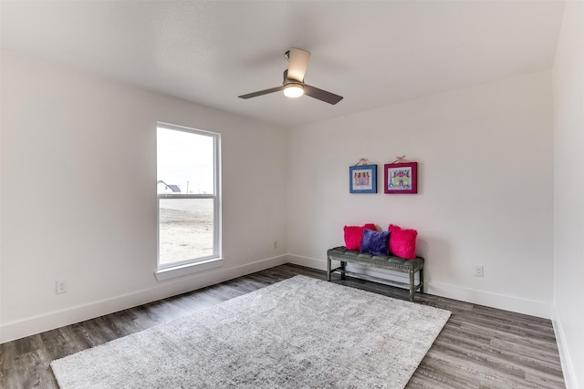 sitting room featuring a ceiling fan, baseboards, and dark wood-type flooring