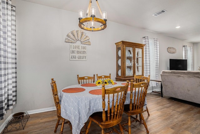 dining area featuring a chandelier, visible vents, baseboards, and wood finished floors