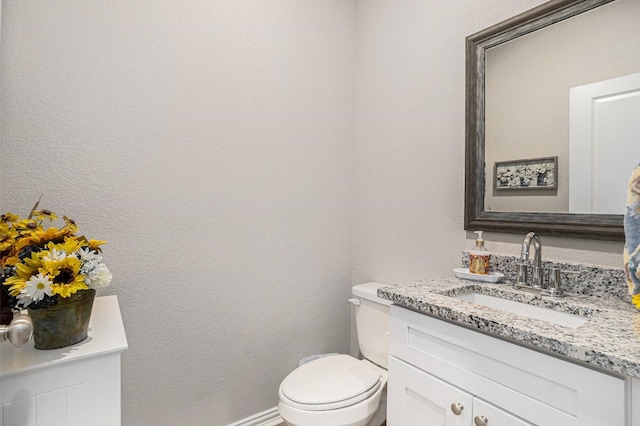 bathroom with a textured wall, vanity, toilet, and baseboards