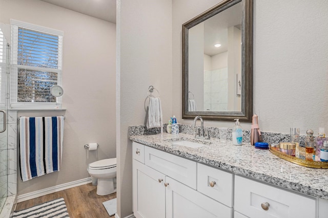 full bathroom featuring toilet, a tile shower, vanity, wood finished floors, and baseboards