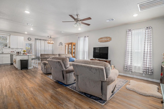 living area with ceiling fan with notable chandelier, visible vents, and wood finished floors