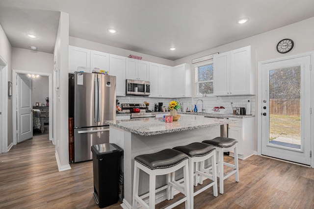 kitchen with a breakfast bar, light stone counters, stainless steel appliances, and wood finished floors