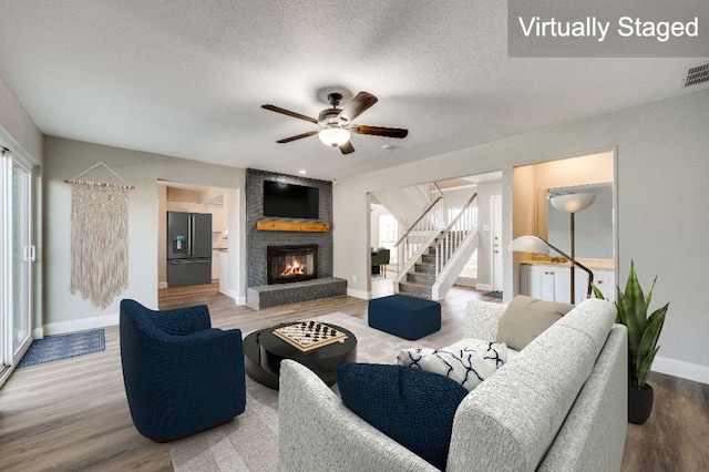 living room featuring ceiling fan, hardwood / wood-style flooring, a fireplace, and a textured ceiling