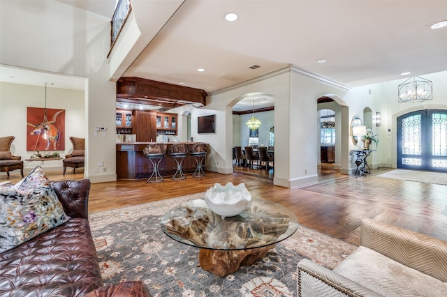 living room with an inviting chandelier, hardwood / wood-style floors, crown molding, and french doors