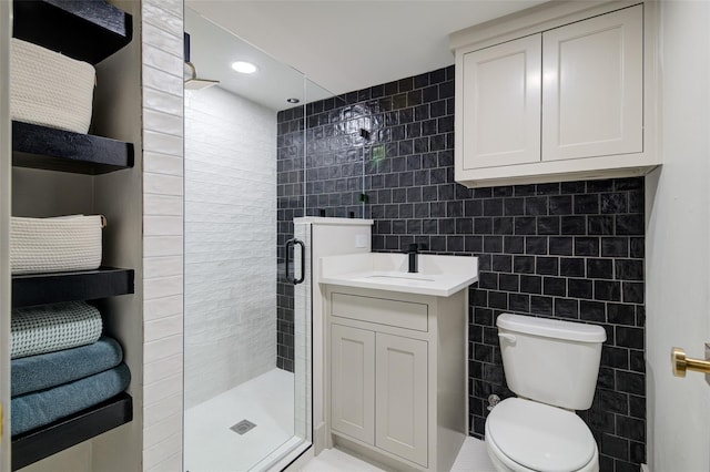 bathroom with a shower with door, vanity, tile walls, and toilet