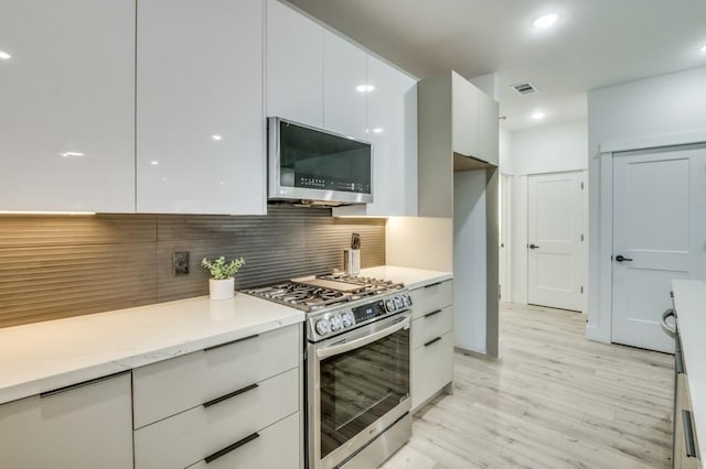 kitchen featuring appliances with stainless steel finishes, light wood-type flooring, decorative backsplash, and white cabinets