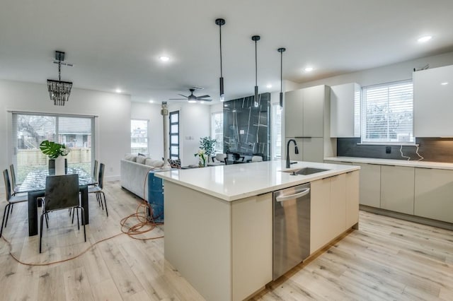 kitchen with sink, light hardwood / wood-style flooring, backsplash, a center island with sink, and decorative light fixtures