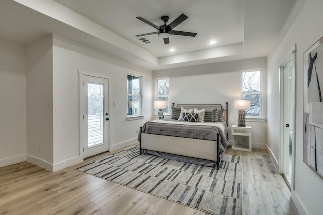 bedroom featuring ceiling fan, a tray ceiling, access to exterior, and light wood-type flooring