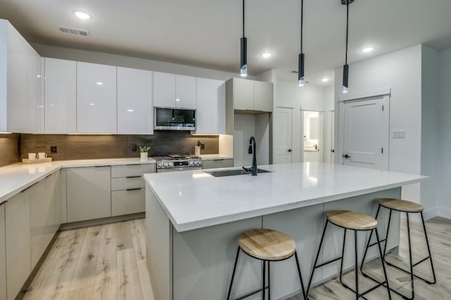 kitchen with white cabinetry, hanging light fixtures, light wood-type flooring, and appliances with stainless steel finishes