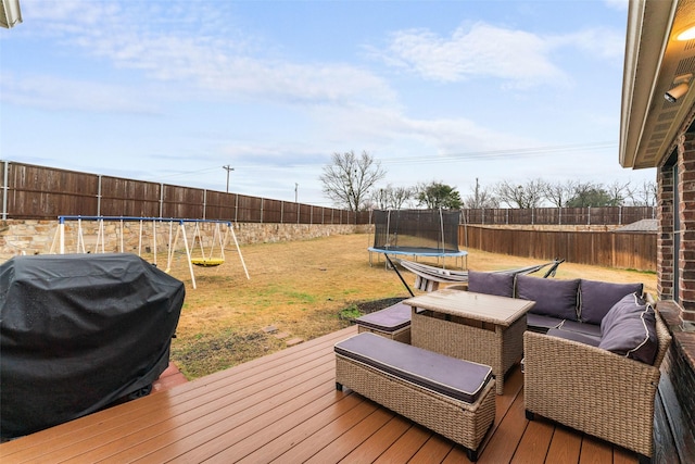 wooden deck featuring a trampoline, a yard, a grill, an outdoor living space, and a playground