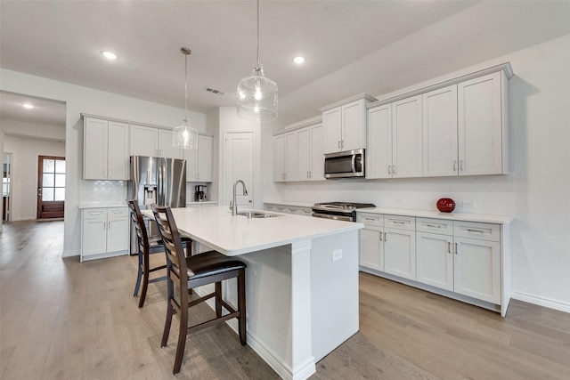 kitchen with appliances with stainless steel finishes, sink, a breakfast bar area, hanging light fixtures, and a center island with sink