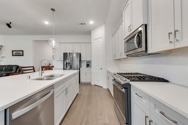 kitchen featuring sink, white cabinetry, stainless steel appliances, decorative light fixtures, and light wood-type flooring