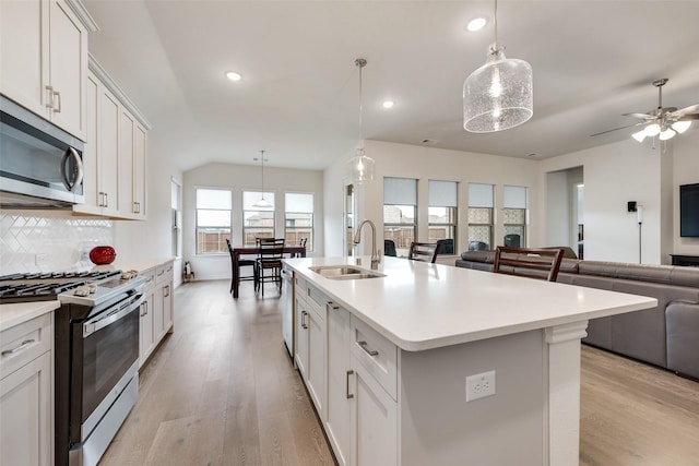 kitchen with an island with sink, white cabinetry, sink, hanging light fixtures, and stainless steel appliances