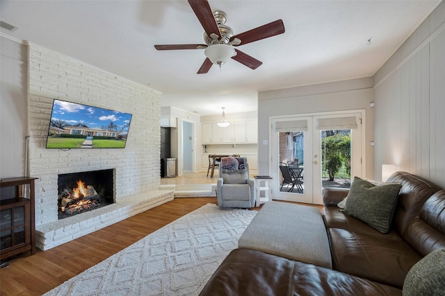 living room featuring a brick fireplace, a ceiling fan, french doors, and wood finished floors