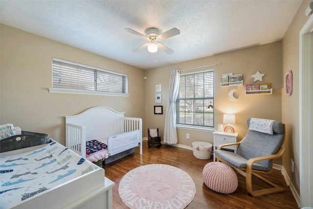 bedroom featuring hardwood / wood-style floors, a nursery area, a textured ceiling, and ceiling fan