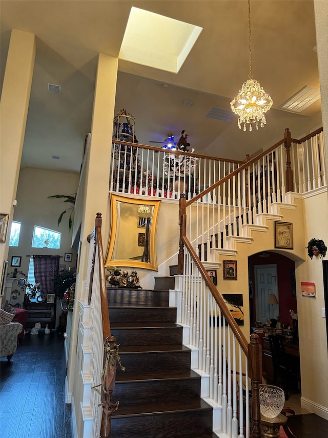 stairway with hardwood / wood-style flooring, ceiling fan with notable chandelier, and high vaulted ceiling