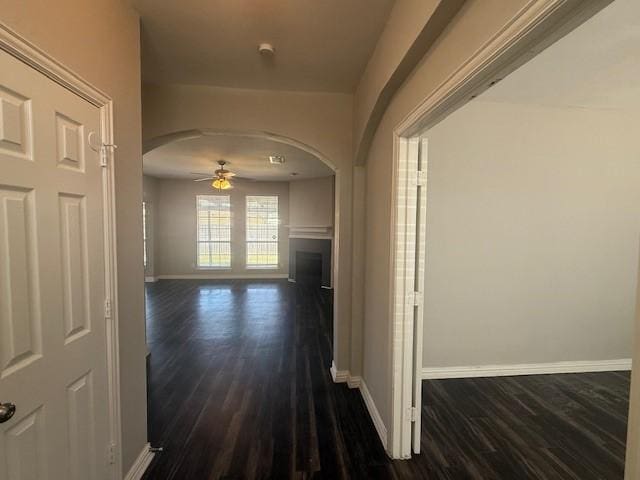 hallway with baseboards, arched walkways, and dark wood finished floors