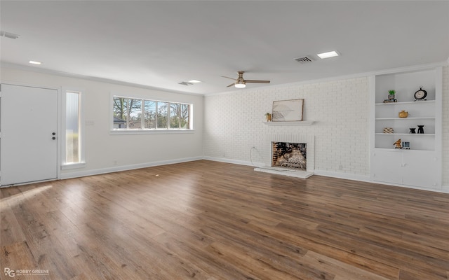 unfurnished living room with a fireplace, visible vents, a ceiling fan, brick wall, and wood finished floors