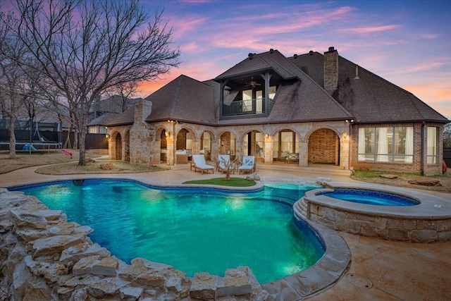 pool at dusk featuring an in ground hot tub, a patio area, and a trampoline