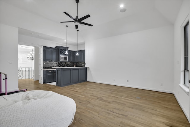 kitchen featuring stainless steel microwave, tasteful backsplash, wood-type flooring, ceiling fan with notable chandelier, and decorative light fixtures