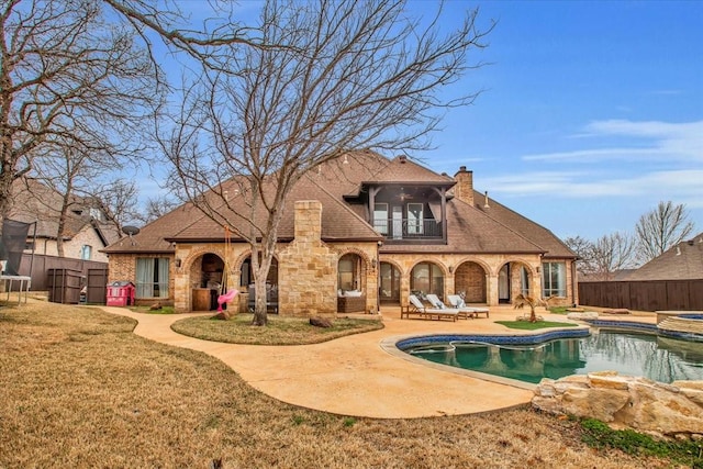 rear view of property with a swimming pool with hot tub, a yard, a patio area, and a balcony