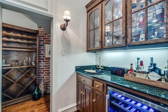 bar with dark wood-type flooring, dark stone counters, beverage cooler, and sink