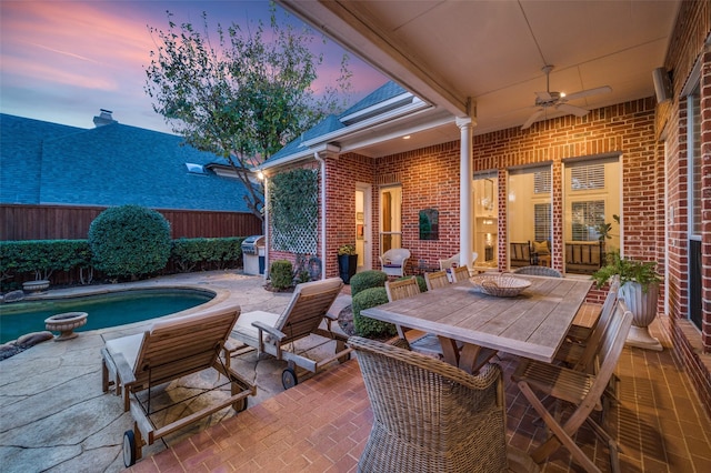 patio terrace at dusk featuring a fenced in pool, grilling area, and ceiling fan