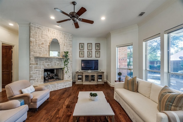 living room featuring ornamental molding, a stone fireplace, dark wood-type flooring, and ceiling fan