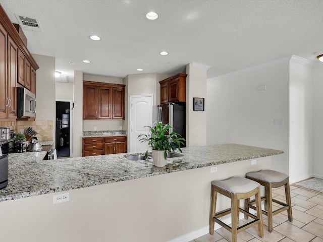 kitchen featuring a peninsula, appliances with stainless steel finishes, visible vents, and light stone countertops