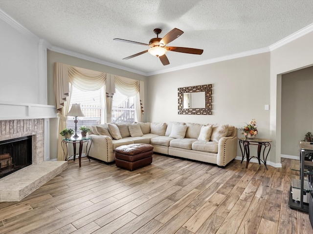 living area featuring a fireplace, light wood-style flooring, ornamental molding, ceiling fan, and a textured ceiling