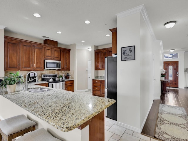 kitchen with light stone counters, stainless steel appliances, a peninsula, a sink, and backsplash